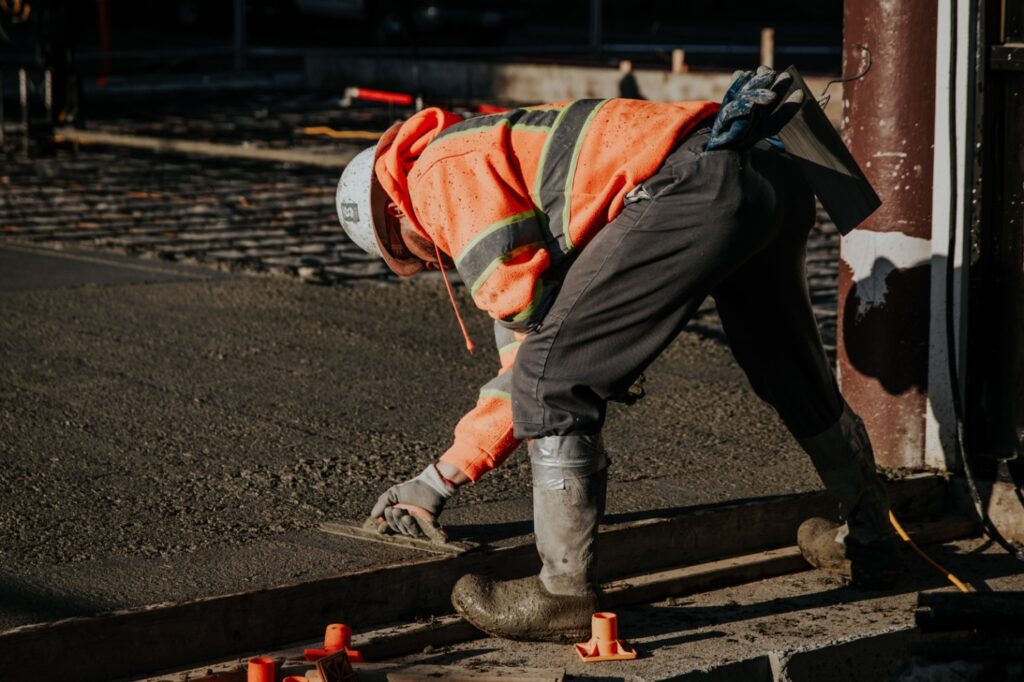 a worker in a hard hat bending and evening wet concrete with a flattening tool