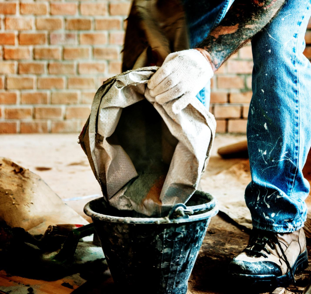 a person, wearing blue jeans, emptying a bag of cement