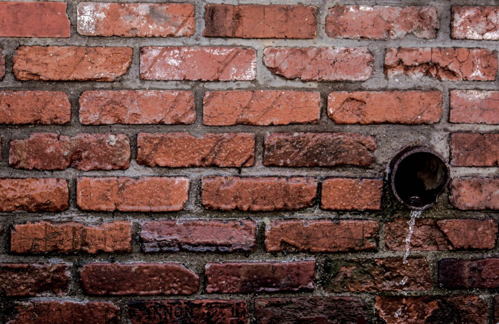 water flowing from a drainage pipe installed in a red brick wall