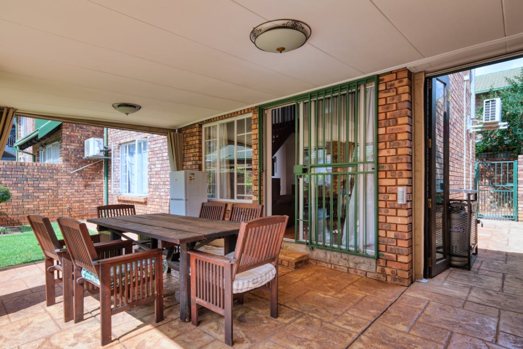 An outdoor patio area with a dining set under a roof adjacent to a brick house