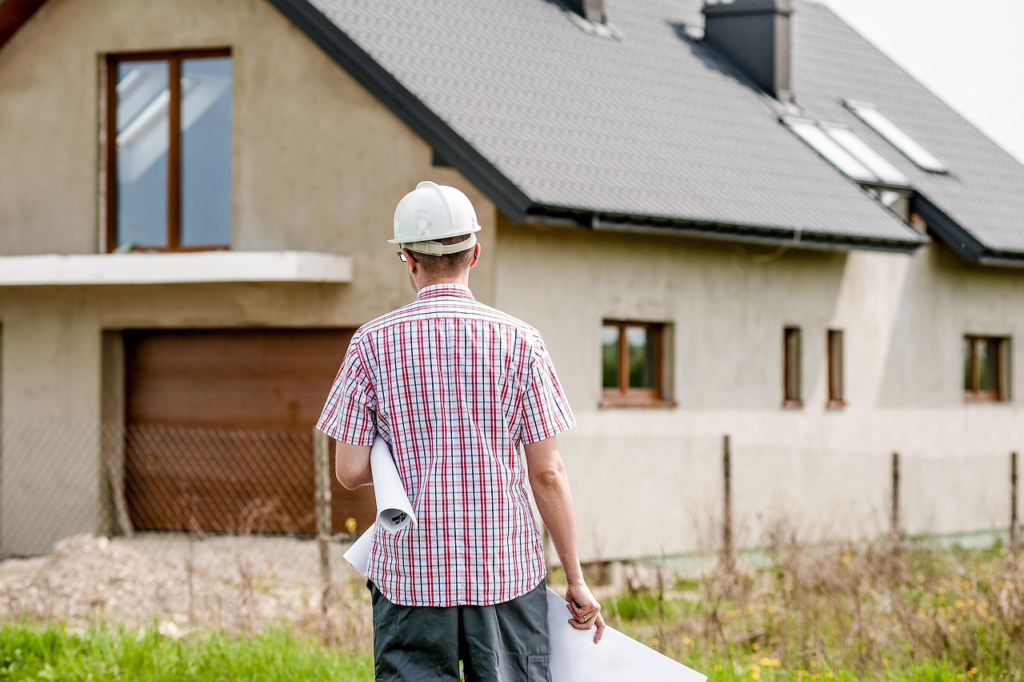 A professional is looking at a house with 2 blueprints in his hand
