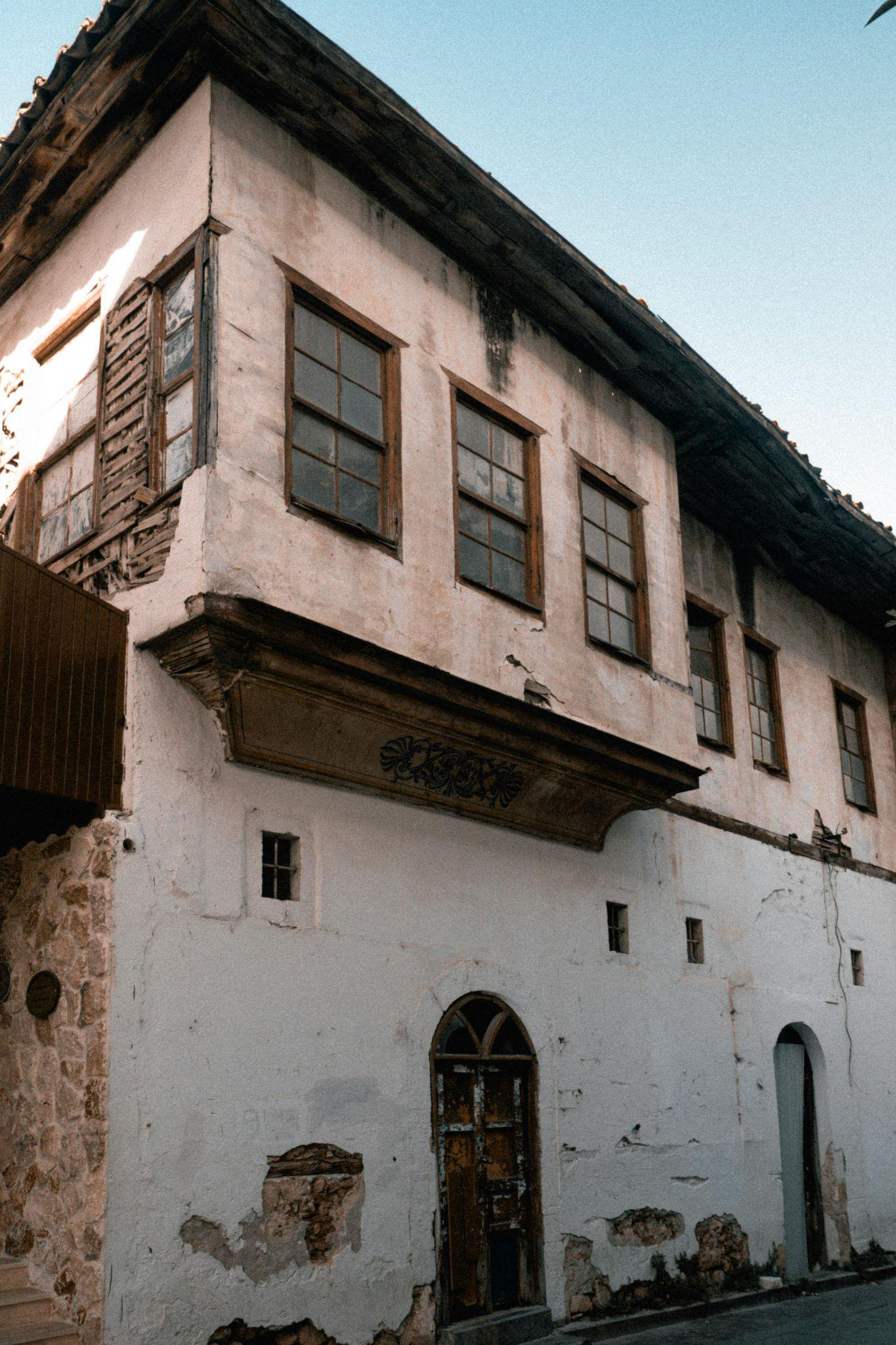 A weathered, two-story masonry house with peeling paint and damaged wooden shutters