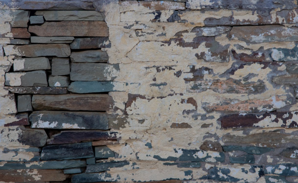 damaged brick wall with grey bricks exposed and wall paint chipping off