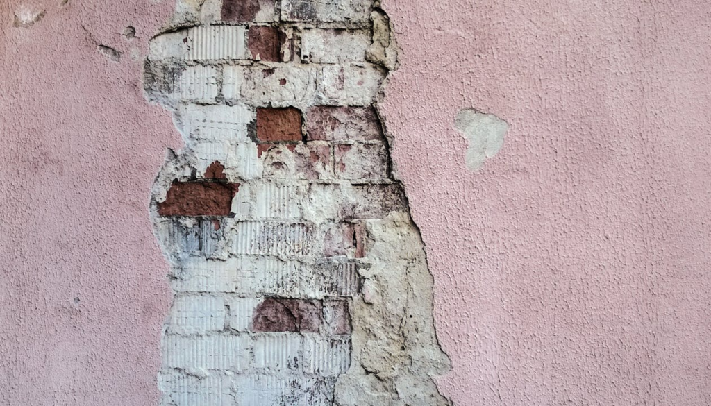 pink wall paint of a wall chipping due to damage and exposing bricks underneath it