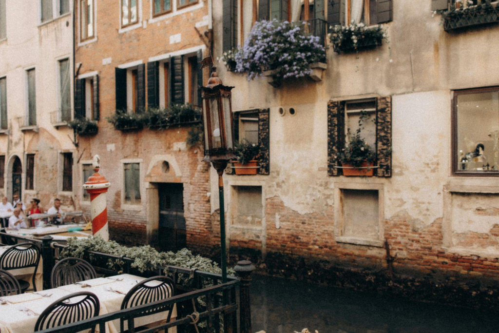 Outdoor café seating along a charming Venetian canal beside aging plaster and brick buildings