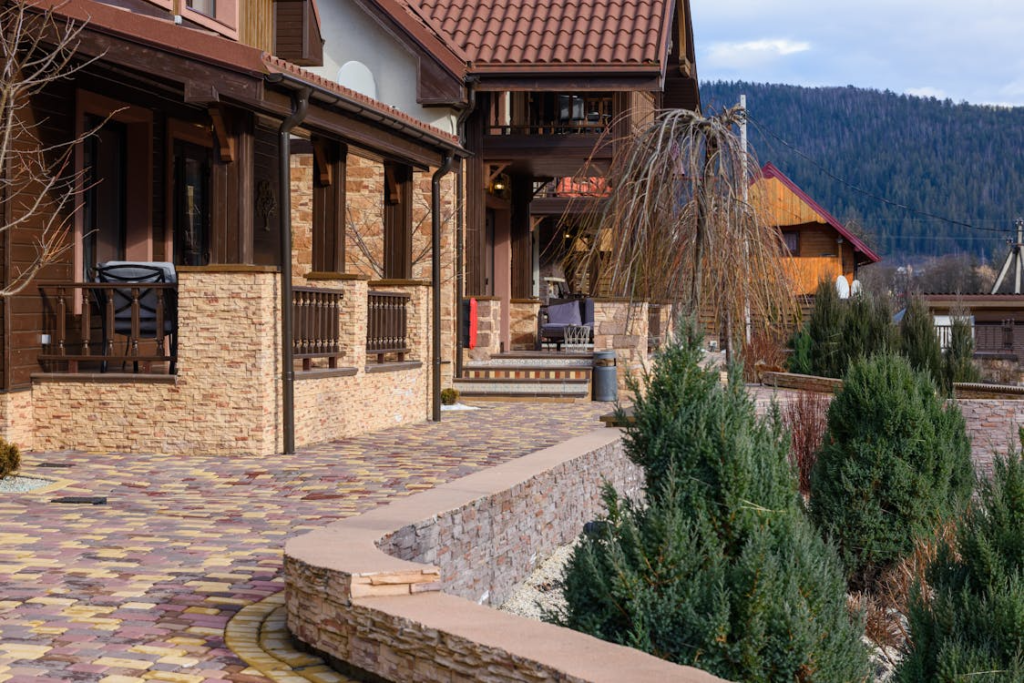 Walkway leading to the front porch of a brown house with a brick exterior, surrounded by landscaped plants