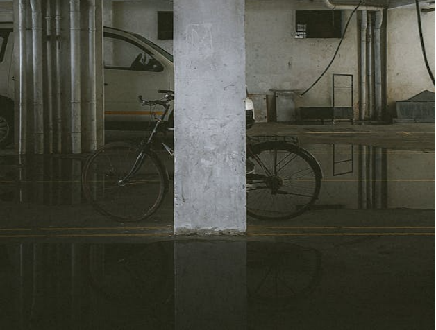 A bicycle and a van are partially obscured by a concrete pillar in a dimly lit parking garage.