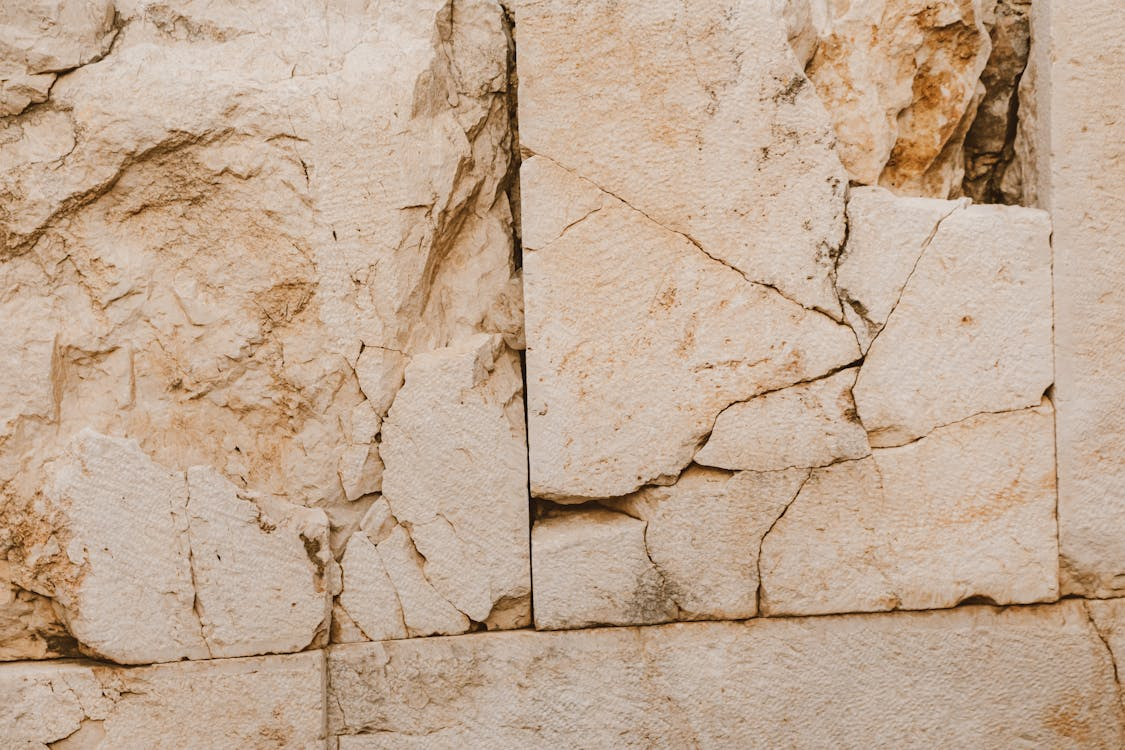 Close-up of a cracked and weathered beige stone wall with visible texture and fissures.