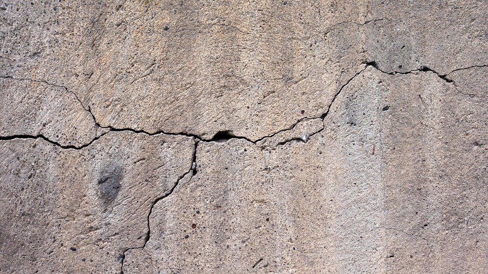 A close-up view of a cracked concrete surface with visible fractures and rough texture.