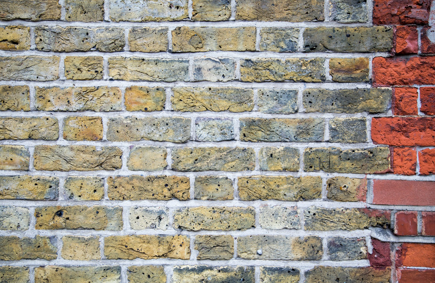 Close-up of a brick wall with faded bricks and a few red bricks at the end