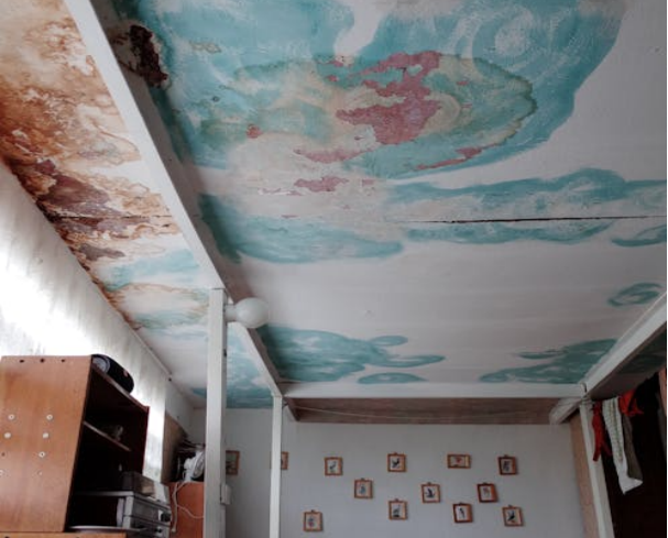 A bedroom with a water-damaged ceiling resembling clouds and personal photos on the walls.