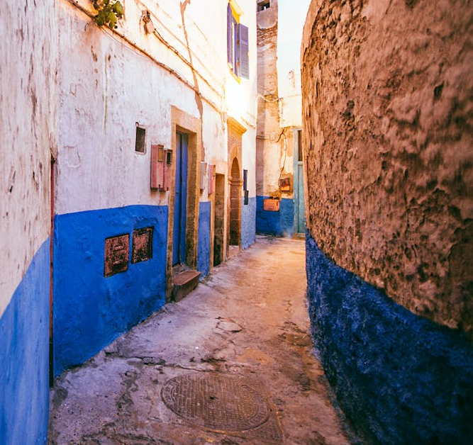 Narrow alleyway with white and blue painted buildings, showing weathered walls and shuttered windows.