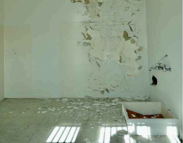 The image shows a room with peeling paint on the walls and a partially broken floor.